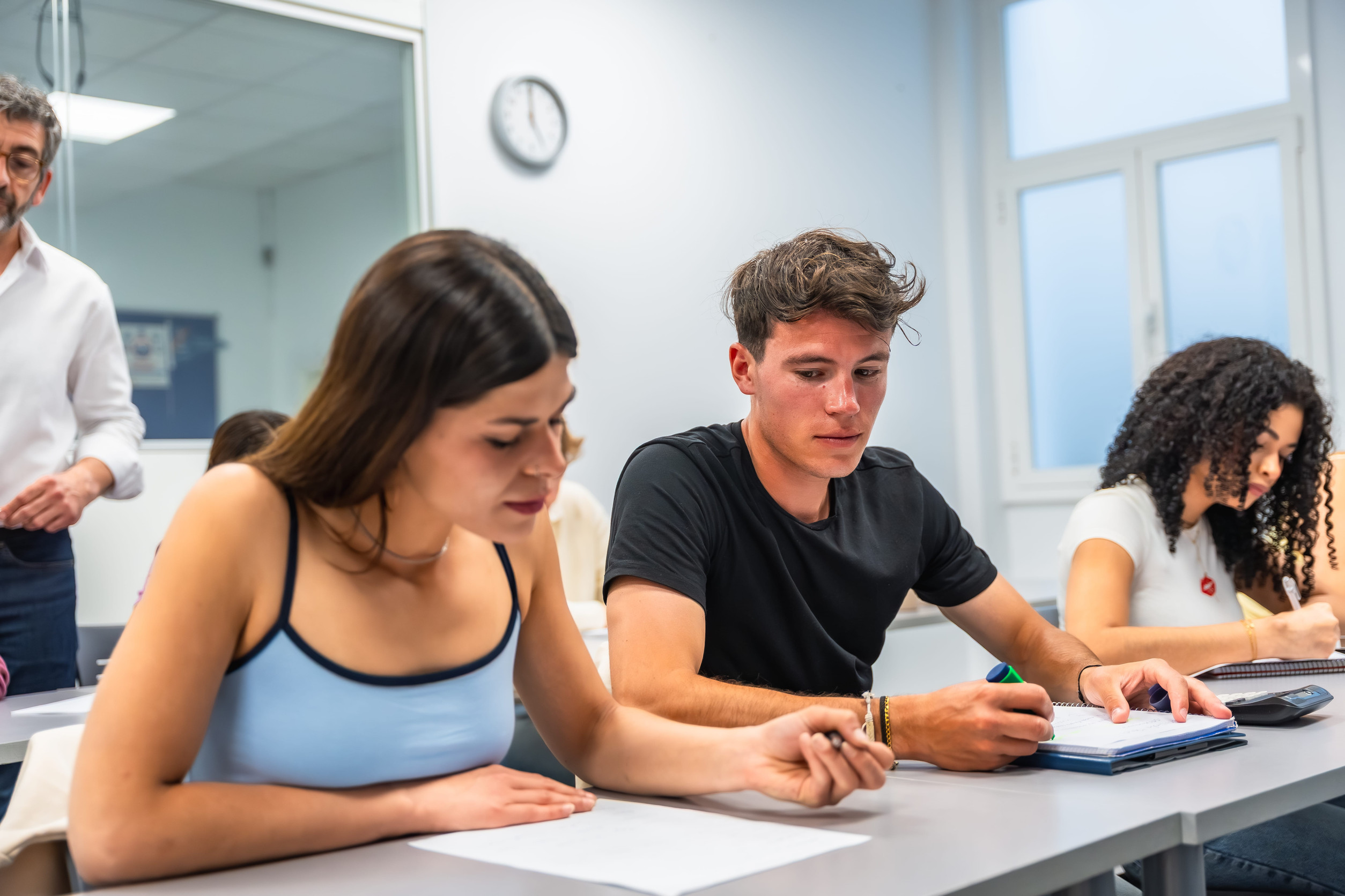 Students are focusing intently on their coursework and writing answers during an important exam or test in a bright classroom while supervised by a teacher. Demonstrating dedication to their education. (File Photo)